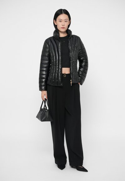 Doudoune noire avec une texture matelassée, fermeture éclair et col haut. Associée à un pantalon large noir et un petit sac à main noir.