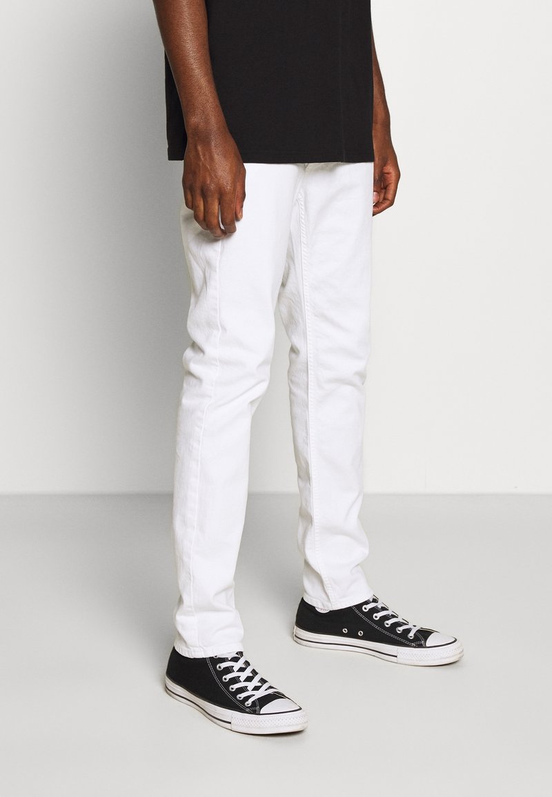 White cotton jeans with a slim fit design, paired with black canvas sneakers featuring white soles and laces. No notable patterns or accents.