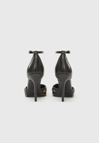 Μαύρα δερμάτινα σανδάλια με ψηλό τακούνι, λουράκια στον αστράγαλο, ανοιχτή πλάτη και χρυσές λεπτομέρειες. Κομψός σχεδιασμός με μυτερή μύτη και τακούνι στιλέτο.