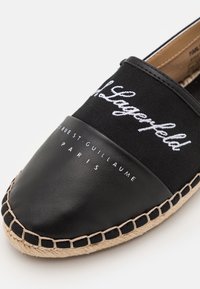 Espadrille noire avec semelle tressée, présentant "Karl Lagerfeld" en écriture blanche et "21 Rue St-Guillaume Paris" imprimé sur la zone des orteils.