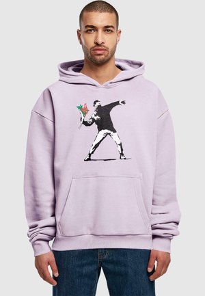 Lilac hoodie with a front pocket features a graphic of a figure throwing flowers. The design includes black and red colors.