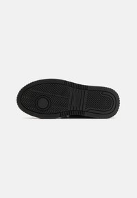Suola di sneaker nera con modelli testurizzati, accenti circolari e una cresta rialzata per la presa. Realizzata in gomma, presenta scanalature prominenti.