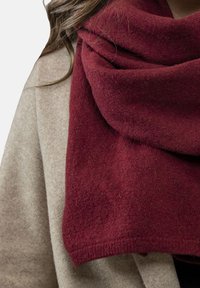 Écharpe en laine bordeaux drapée sur un manteau beige, mettant en valeur une texture douce et un design large et enroulé.