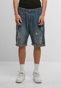 Shorts en denim de couleur bleu clair avec un design déchiré, présentant des accents déchirés et des ourlets retroussés. Assortis à des baskets blanches et des chaussettes.