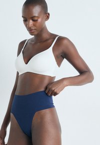 Witte draadloze bh met een diepe decolletélijn, gecombineerd met marineblauwe high-waisted onderbroek. Gladde textuur, minimalistisch ontwerp, geen zichtbare hardware.