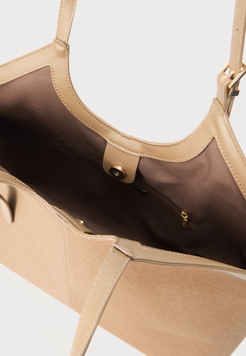 Bolso tote beige con exterior de cuero liso e interior suave. Cuenta con un bolsillo con cremallera y correas resistentes para facilitar su transporte.