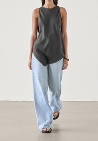 Czarny bezrękawnik z okrągłym dekoltem, w połączeniu z luźnymi, jasnoniebieskimi dżinsami i czarnymi sandałami. Gładka tekstura, casualowy styl.