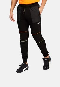 Joggers negros con un ajuste slim, que cuentan con dos bolsillos laterales, acentos rojos y verdes, y puños elásticos. Fabricados con un material suave y elástico.