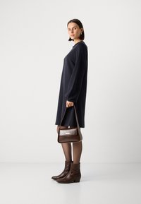Donkerblauwe oversized jurk met lange mouwen, gecombineerd met bruine leren enkellaarsjes en een bijpassende bruine handtas met een sluiting.