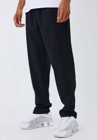 Pantaloni neri a maglia con un design svasato, abbinati a scarpe sportive bianche con tacco visibile e dettagli perforati.