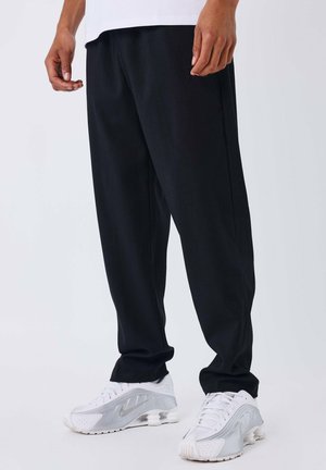 Pantaloni neri a maglia con un design svasato, abbinati a scarpe sportive bianche con tacco visibile e dettagli perforati.