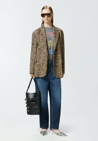 Blazer con stampa leopardata sopra una t-shirt grafica, abbinato a jeans a gamba larga blu e scarpe con tacco argento. Accessoriato con una borsa nera.