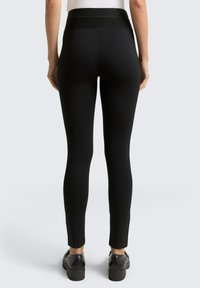 Zwarte legging met een brede, gestructureerde tailleband. Ze hebben een slim fit en een gladde afwerking, met een taps toelopende pijp naar de enkel.