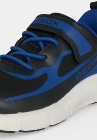 Gros plan sur une basket Geox noire et bleue avec des lacets bleus, une bride velcro bleue, un matériau en mesh et une épaisse semelle blanche.