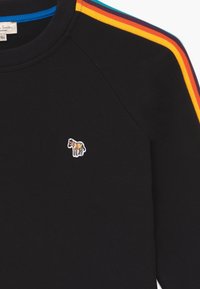 Černá mikina s barevnými pruhy podél ramen. Na hrudi má vyšívané logo koně. Jemná textura.