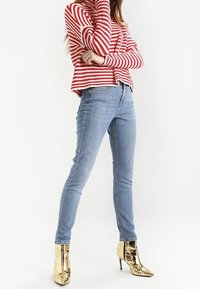 Červeno-bílý pruhovaný svetr, volný střih, doplněný o světle modré úzké džíny a lesklé zlaté vysoké kotníkové boty.