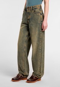 Lätta blekta gröna denimjeans med vida ben och hög midja, fem fickor, kontrasterande sömmar och avslappnad passform, ihop med bruna skor.