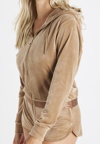 Tan lynlås-hættetrøje i blødt velourstof med hætte, med en mærkevarebronze elastisk taljebånd og dekorativ lynlåstrækker.