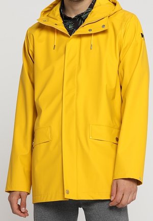 Homme portant une veste de pluie à capuche jaune vif avec des poches à boutons-pression et une fermeture éclair dissimulée par un rabat coupe-vent.