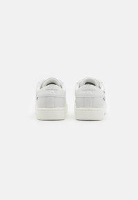 En par vita Calvin Klein Jeans-sneakers som visas från baksidan, med en ren design och logga på hällorna mot en vit bakgrund.