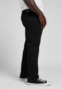 Czarne dżinsy o prostym kroju, z subtelnymi detalami szwów i markowym paskiem. Noszone z czarno-białymi trampkami.