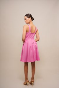 Rosa ärmelloses Kleid mit tailliertem Oberteil und schwingendem Rock. Weicher Stoff, Rücken freigelegt, mit Knopfdetails. Goldene High-Heels.