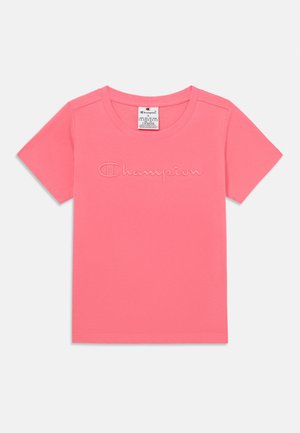 Camiseta de algodón de color rosa claro con cuello redondo y mangas cortas. Presenta un logo de "Champion" bordado en la parte frontal. Textura suave.