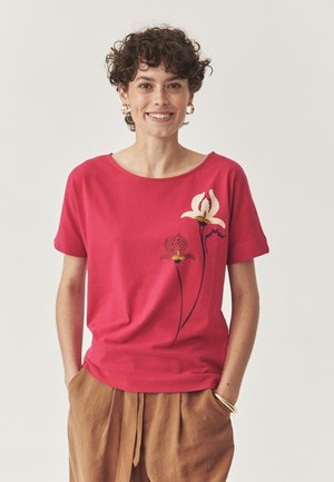 T-shirt en coton rouge à manches courtes, ornée de motifs floraux en crème, violet foncé et jaune sur le côté gauche. Coupe décontractée.
