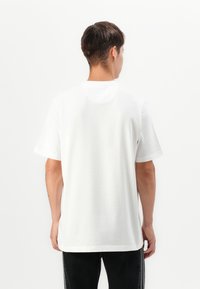 T-shirt bianco a maniche corte realizzato in morbido cotone, con colletto a girocollo classico e vestibilità rilassata, mostrato da dietro.