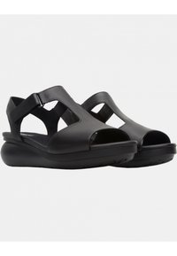 Sandali in pelle nera con punte aperte, caratterizzati da una suola curva e fasce larghe. Fibbia regolabile per una vestibilità sicura. Texture liscia.