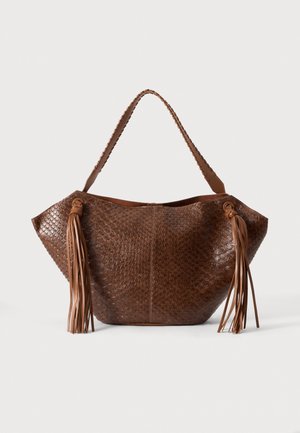 Sac à bandoulière en cuir marron texturé, avec une poignée tressée et de longues pampilles de chaque côté, sur un fond uni.