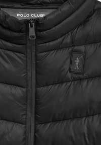 Sort polstret vest med høj krave, der har en lodret lynlås. Omfatter et tekstureret logo-patch på brystet. Glat, blankt stof.