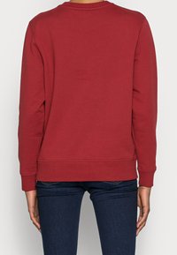 Sudadera roja de manga larga, con un cuello redondo acanalado y una cintura. Hecha de un tejido suave, presenta un diseño liso sin acentos adicionales.