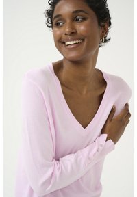 Maglione rosa chiaro a scollo a V realizzato in materiale morbido, con dettagli di bottoni sui polsini e una vestibilità comoda, mostrando una texture liscia.