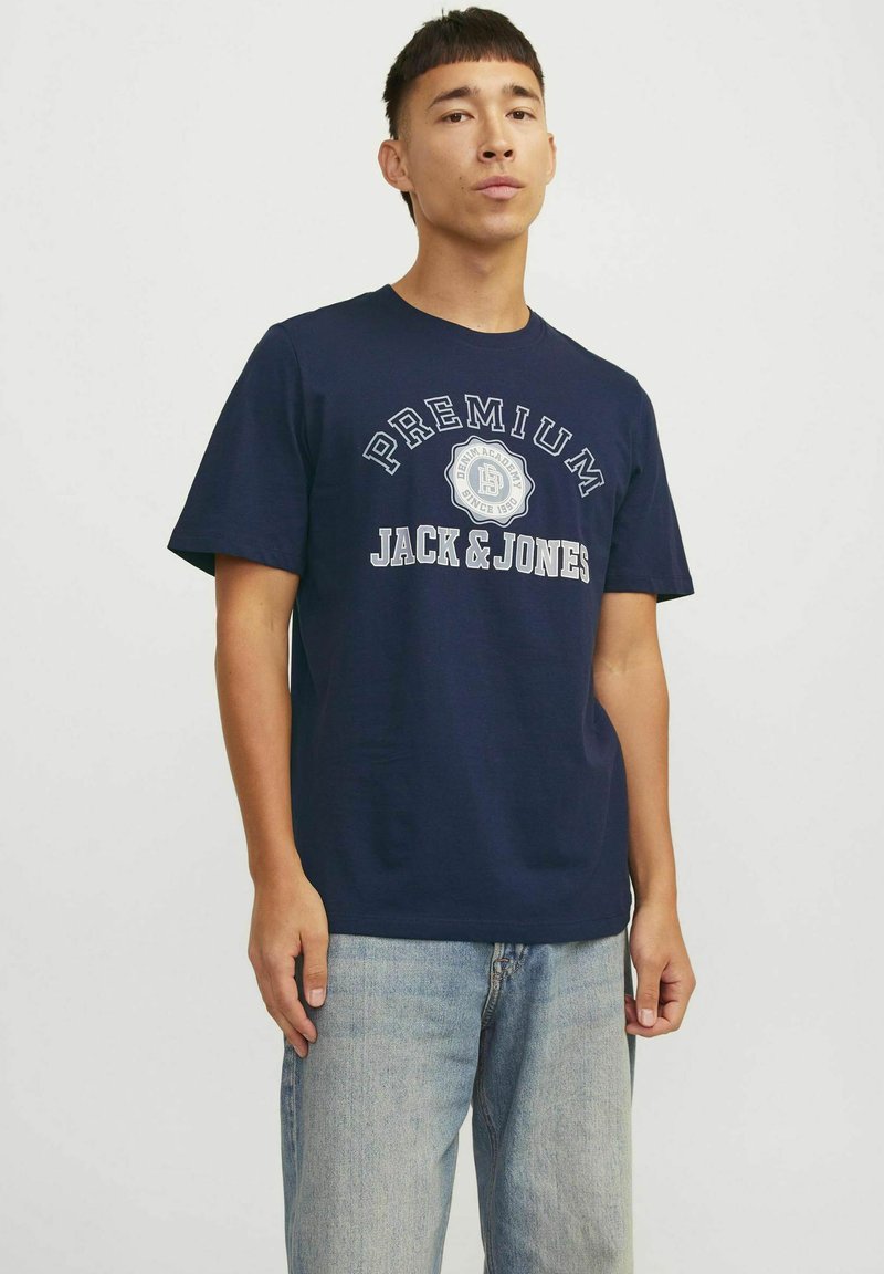 Tamno plava pamučna majica s bijelim tekstom "PREMIUM JACK & JONES". Kratki rukavi, okrugli izrez i opušteni kroj. Uparena s svijetloplavim trapericama.