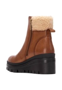 Bota de tobillo de cuero marrón con un puño de piel de oveja, cremallera lateral y suela negra gruesa con un patrón de textura en la superficie.