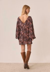 Vestido con estampado floral, con un profundo escote en forma de V en la espalda, mangas largas abullonadas y corte recto. Tonos terrosos de azul oscuro, rosa y marrón. Botas marrones hasta la rodilla.