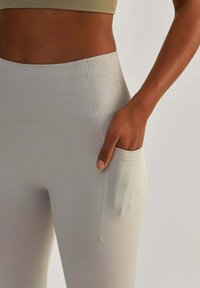 Leggings alti in grigio chiaro con texture a costine, dotati di una tasca laterale e dettagli di cucitura sottili. Tessuto morbido ed elastico.