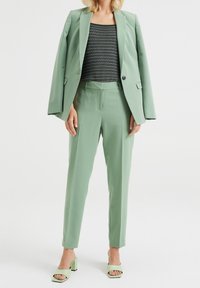 Zelený blazer a odpovídající kalhoty z hladkého materiálu, zkombinované s topem s černobílými pruhy a sandály s blokovým podpatkem v mentolově zelené barvě.