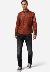 Brun læder skjorte med knaplukning fortil, to brystlommer og krave, parret med mørke denim jeans og sorte sneakers.