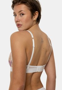 Soutien-gorge en dentelle florale blanche avec des bretelles réglables et une fermeture à crochet au dos, doté de détails raffinés et d'une finition lisse.