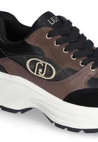 Grube sneakersy w kolorze czarnym, brązowym i z zamszu, z czarnymi sznurowadłami, białą podeszwą oraz złotym owalnym logo na bocznej części.