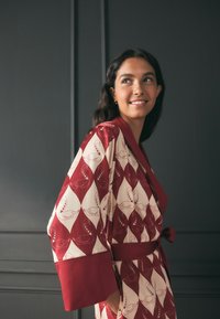 Punase ja kreemikad mustriga kimono, millel on luigemotiivid, laiad varrukad, seotud vöö ja tekstuuriga kangas. Aksentvärvid täiustavad disaini.