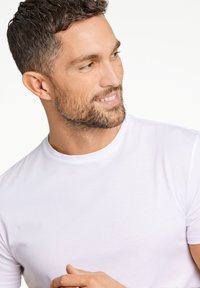 T-shirt bianco in cotone con scollatura rotonda e maniche corte, caratterizzato da una superficie liscia e un design minimalista. Senza motivi o accenti.