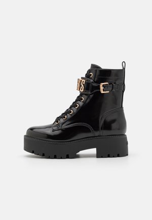 Bottes de combat en cuir verni noir avec quincaillerie dorée, devant à lacets, épaisse plateforme noire et sangle décorative avec détail de logo.