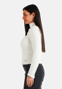 Weißer gerippter Pullover mit hohem Ausschnitt und langen Ärmeln, der über eine weiche Textur und ein kurzes Design verfügt. Dezentes Logo-Detail am Saum.