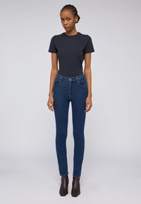 Mörkblå skinny jeans med hög midja, med framfickor och kontrasterande sömmar, i kombination med en åtsittande svart t-shirt och ankelskana.
