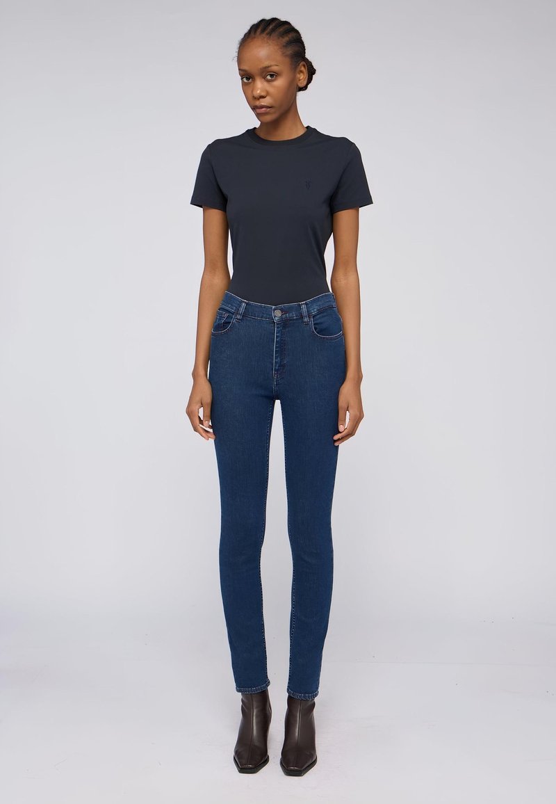 Mörkblå skinny jeans med hög midja, med framfickor och kontrasterande sömmar, i kombination med en åtsittande svart t-shirt och ankelskana.