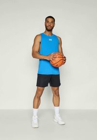 Blaues ärmelloses Sportshirt, schwarze Shorts, hält einen orangefarbenen Basketball. Weiße Sneaker mit strukturierten Sohlen und weißen Sportsocken.