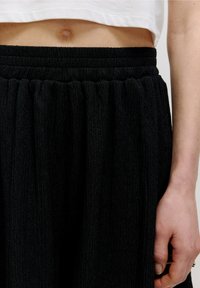 Pantaloni larghi neri con texture e vita elasticizzata. Il tessuto presenta un aspetto arricciato, con profondità e pieghe morbide.